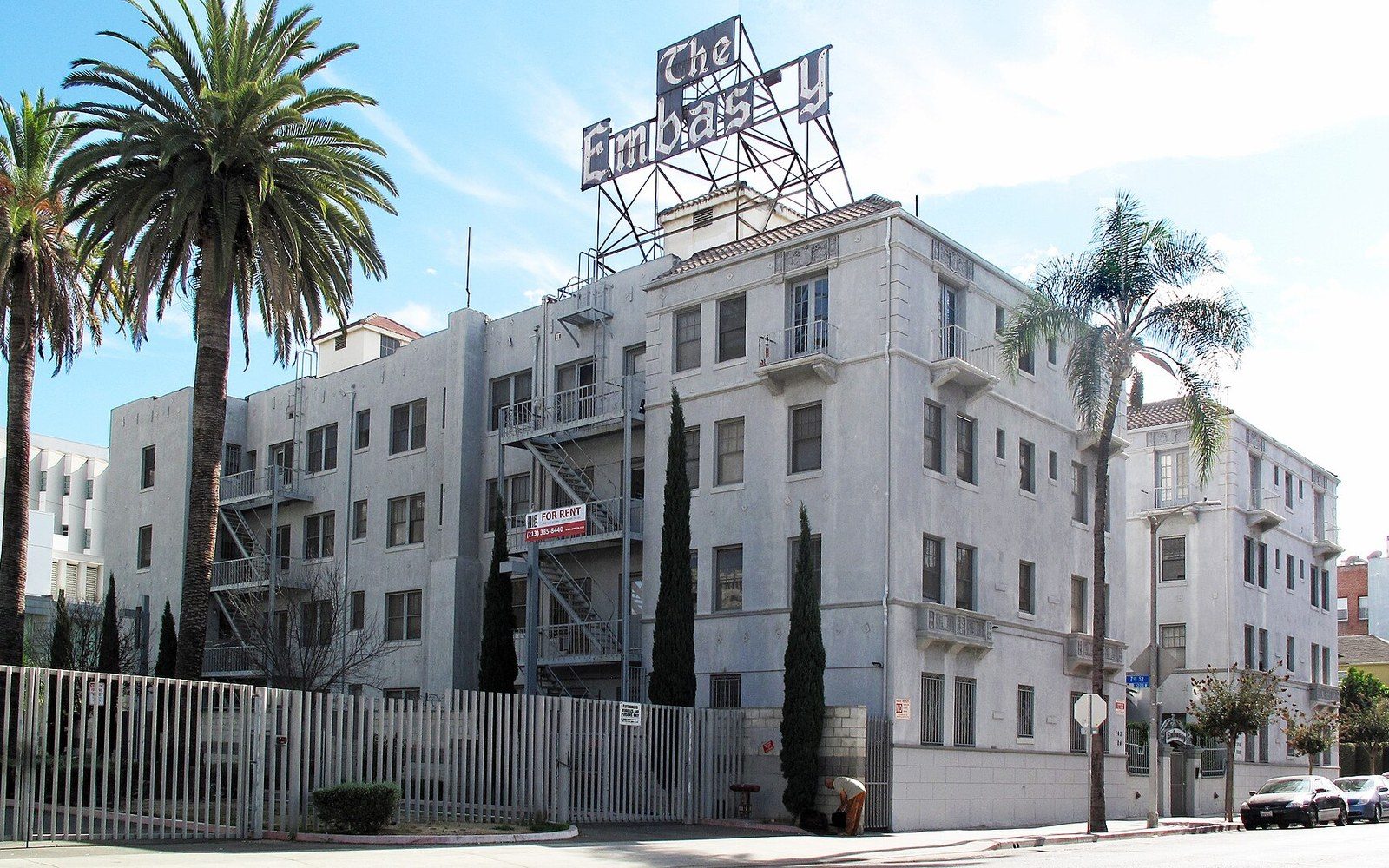 The Embassy building's rooftop sign rises above a white multi-story building with palm trees